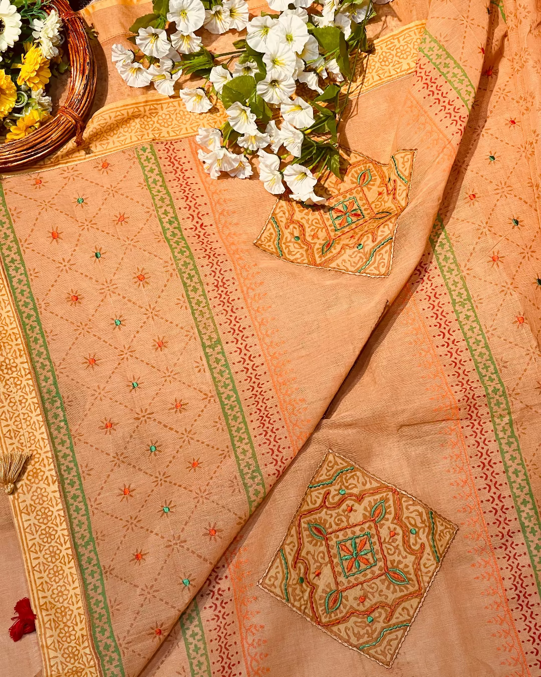 Decorative fabric with intricate patterns and a basket of flowers on a textured surface.