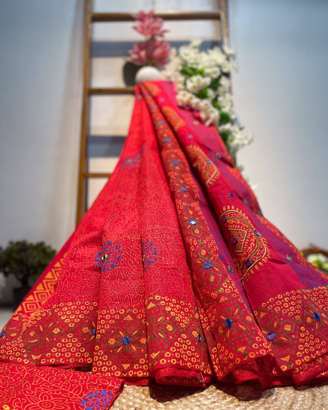 Red embroidered fabric with intricate patterns draped over a wooden ladder.