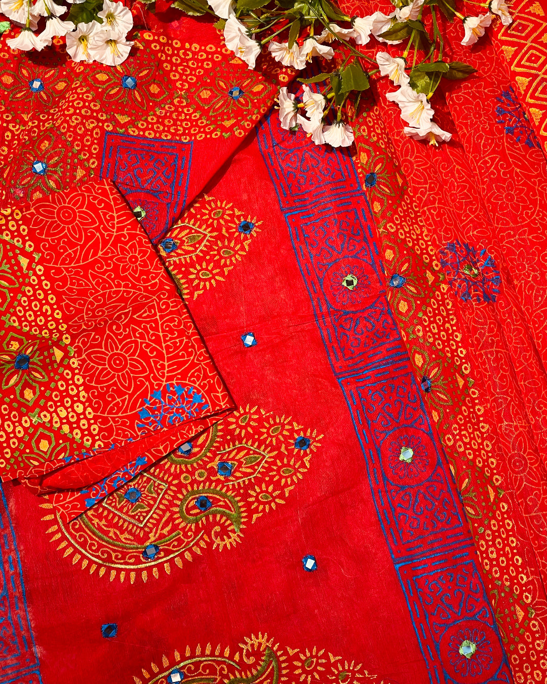 Red fabric with blue and gold patterns and white flowers on a red background