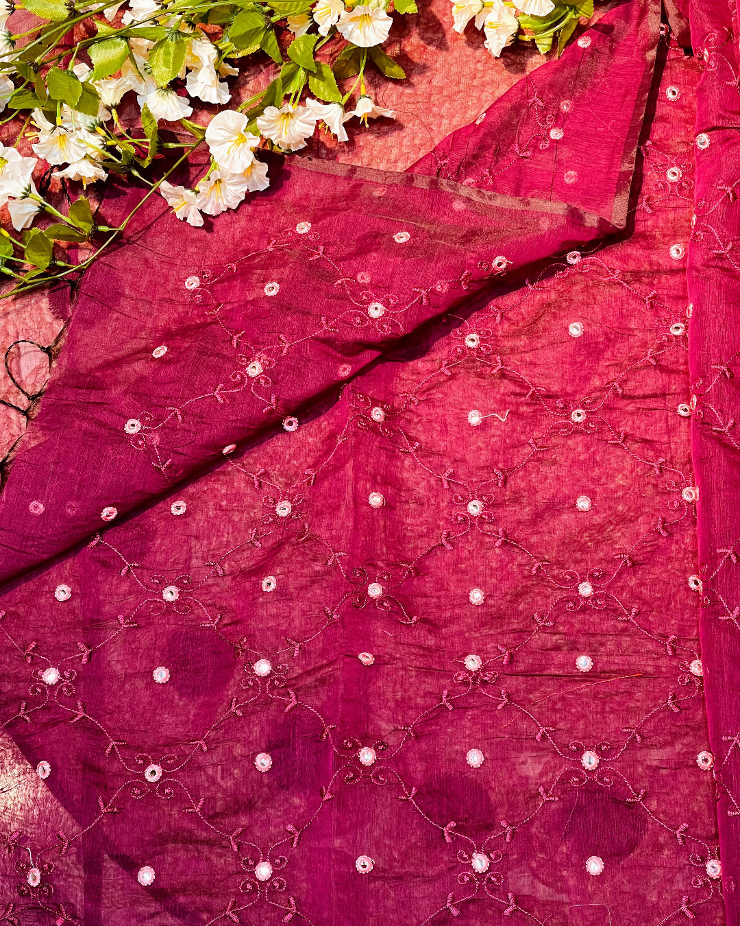 Close-up of a pink embroidered fabric with white flowers and green leaves.
