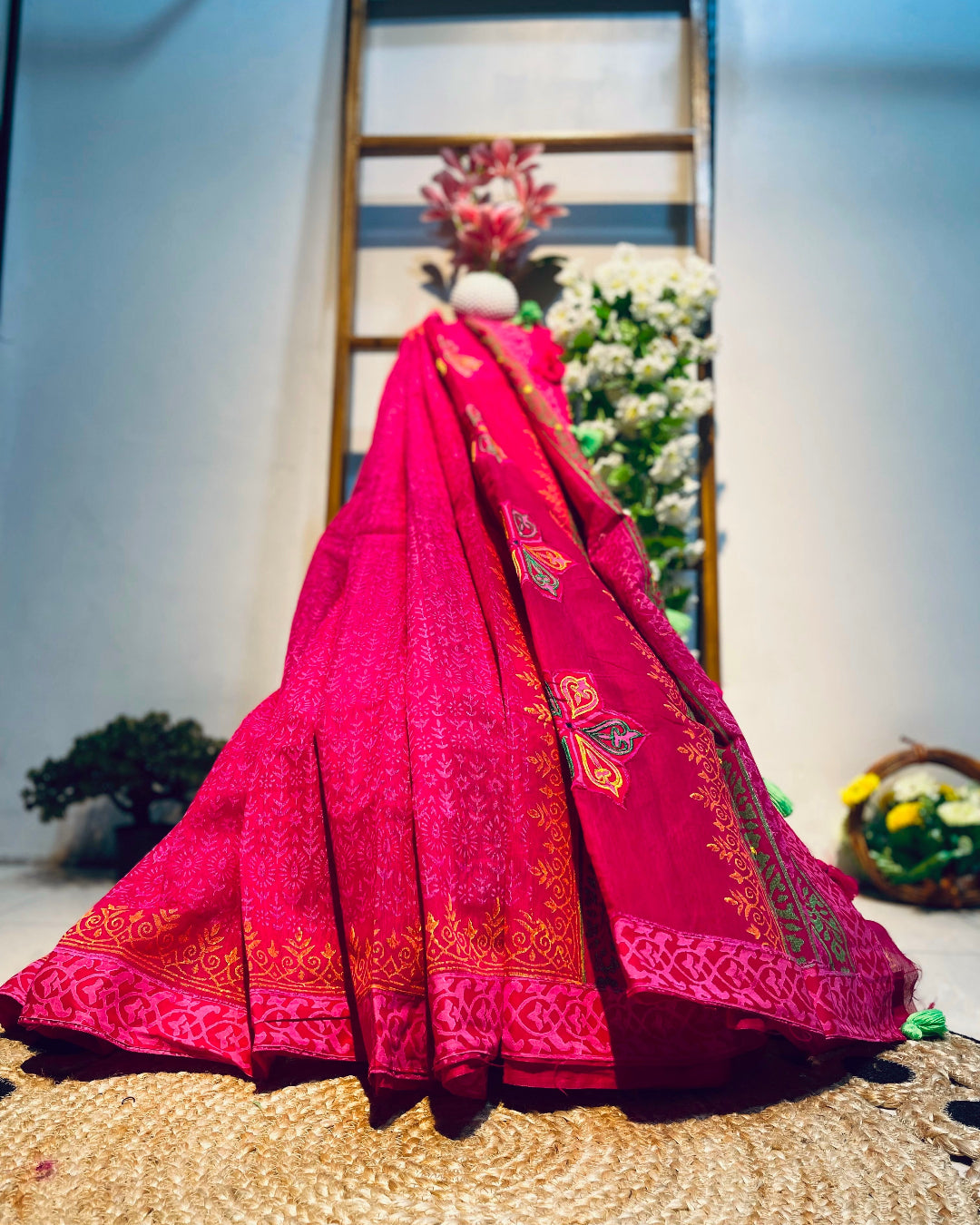 Pink embroidered saree on a mannequin against a floral backdrop