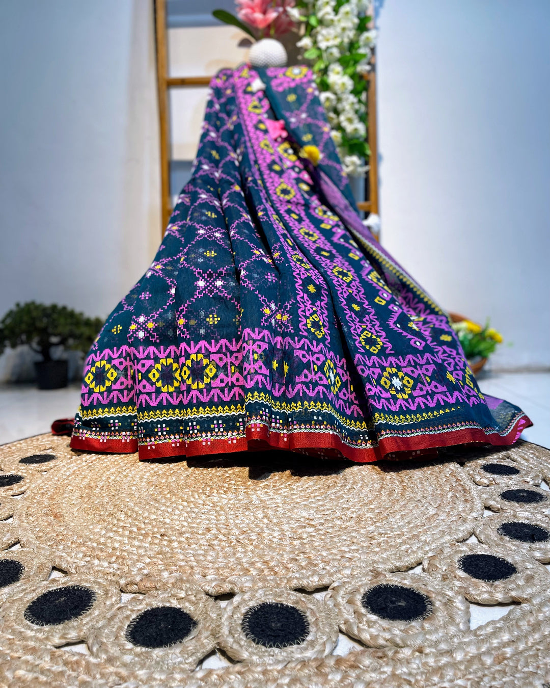 Colorful embroidered fabric draped over a woven surface with a blurred floral background
