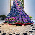 Colorful embroidered fabric draped over a woven surface with a blurred floral background