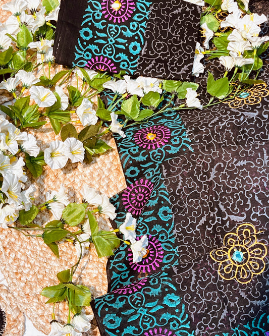 Black fabric with colorful patterns on a textured surface with white flowers and green leaves.
