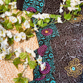 Black fabric with colorful patterns on a textured surface with white flowers and green leaves.