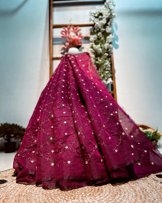 Magenta embroidered saree on a decorative stand with flowers in the background