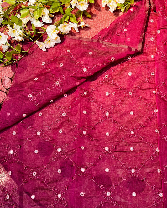 Close-up of a pink embroidered fabric with white flowers and green leaves.