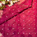 Close-up of a pink embroidered fabric with white flowers and green leaves.